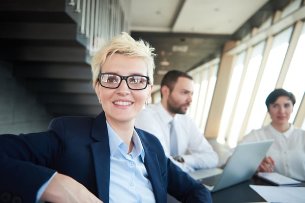 blonde with short hairstyle  and glasses,  business woman on meeting, people group in background at modern bright office indoors
